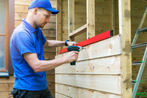 shed upgrade construction - worker installing wooden facade planks